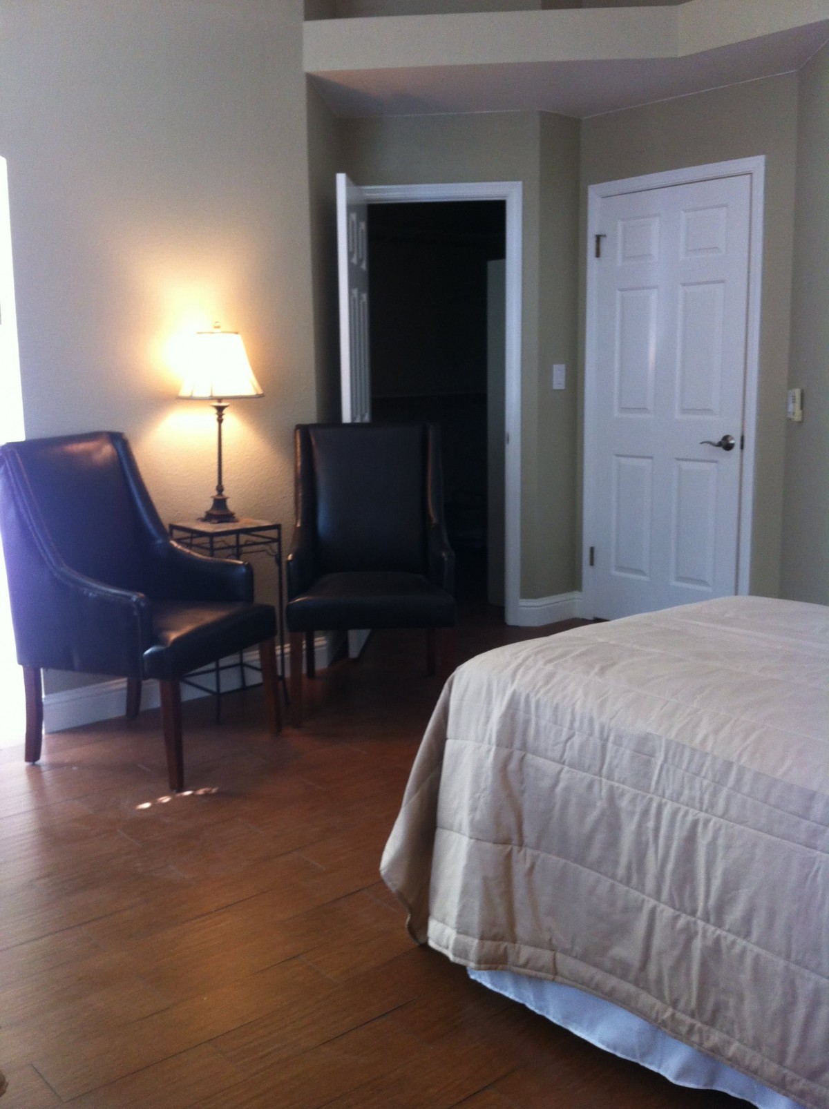 A cozy bedroom with a bed, two chairs, a lamp, and a door.
