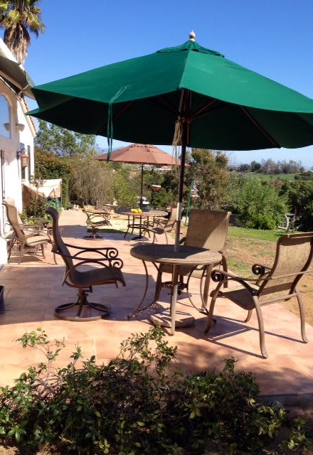 A sunny patio with outdoor furniture and a green umbrella.