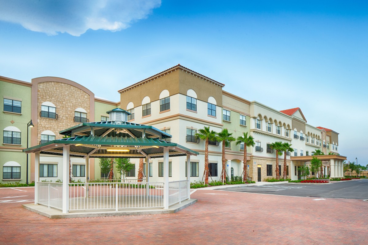 A modern, multi-story building with palm trees and a gazebo under a clear blue sky.