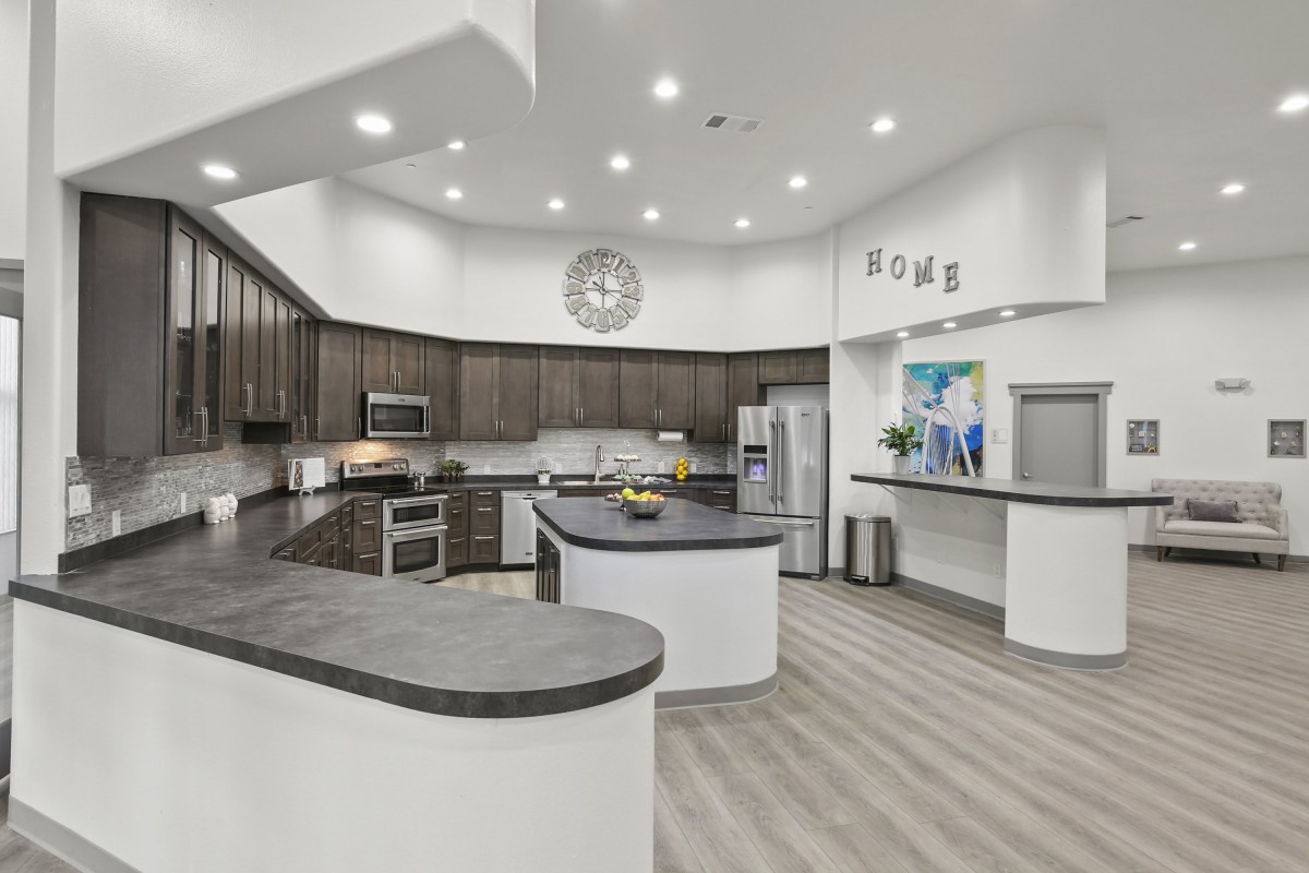 Modern kitchen with a central island, stainless steel appliances, and wood cabinets under recessed lighting.