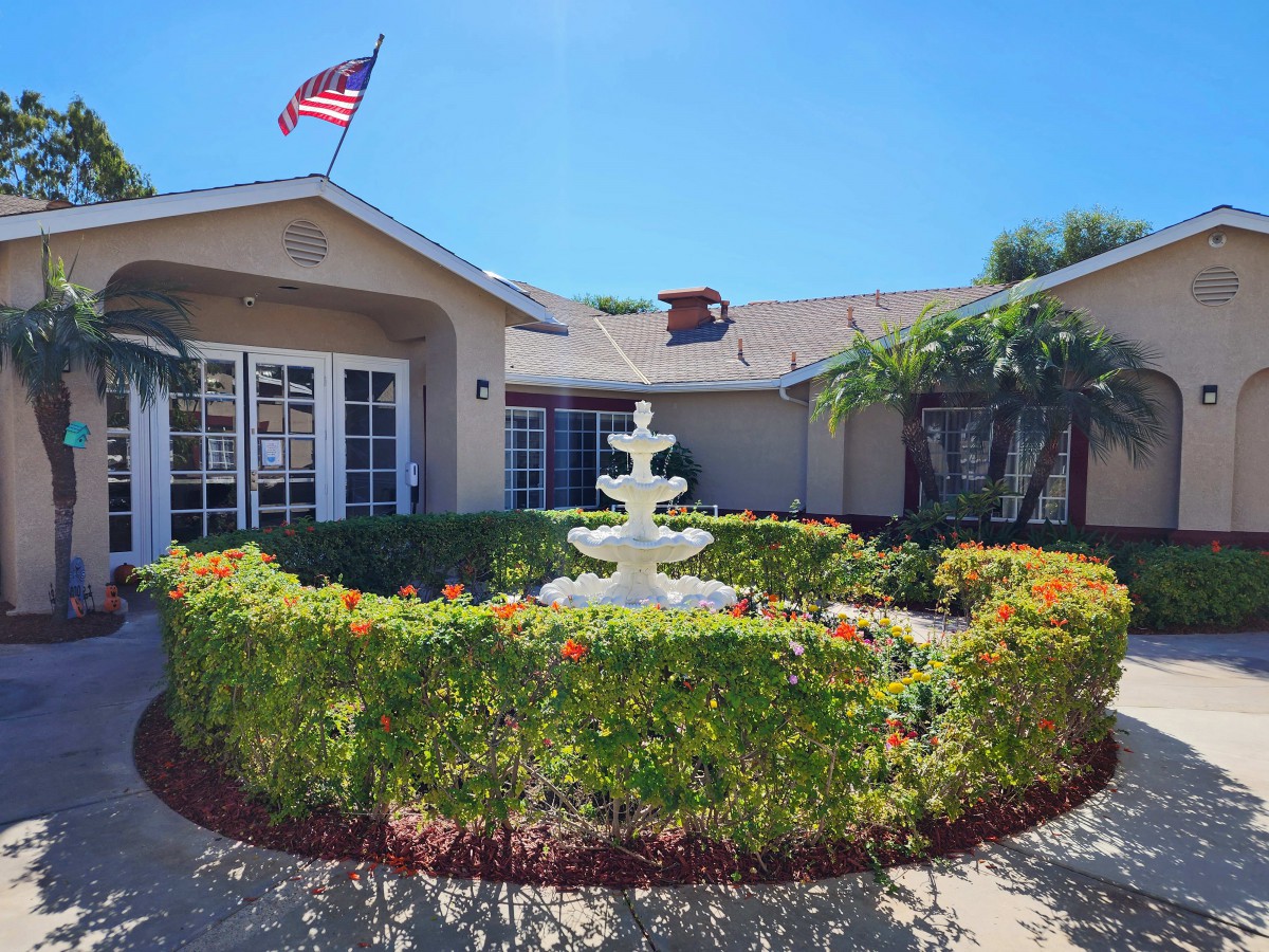 A peaceful garden with a central fountain in front of a building, adorned with an American flag on a sunny day.