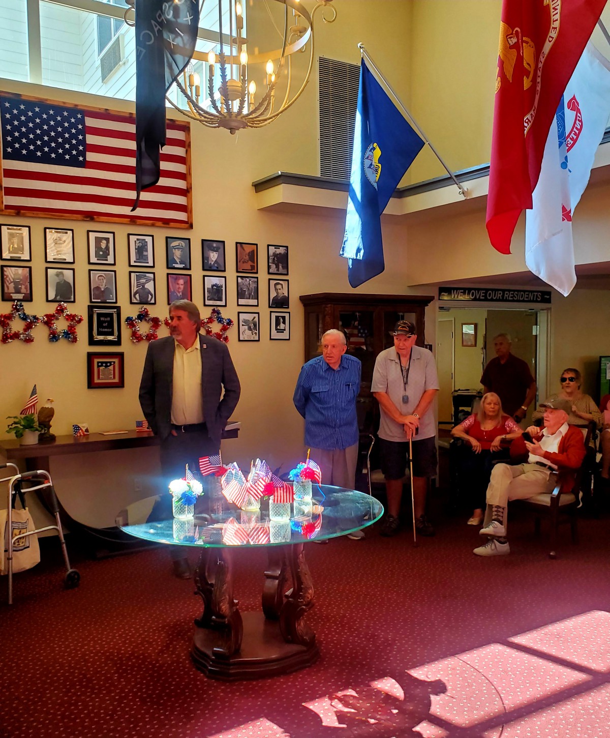 A group of people standing in a room decorated with flags and framed portraits, possibly during a ceremonial event.