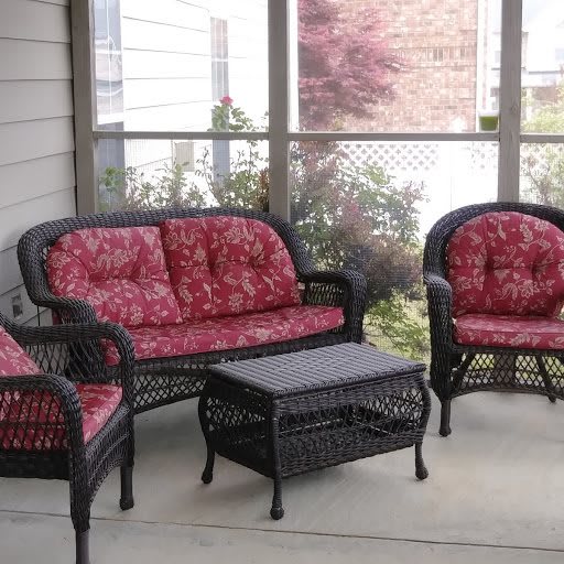 A cozy patio setup featuring a wicker loveseat, two matching chairs with red cushions, and a small coffee table.