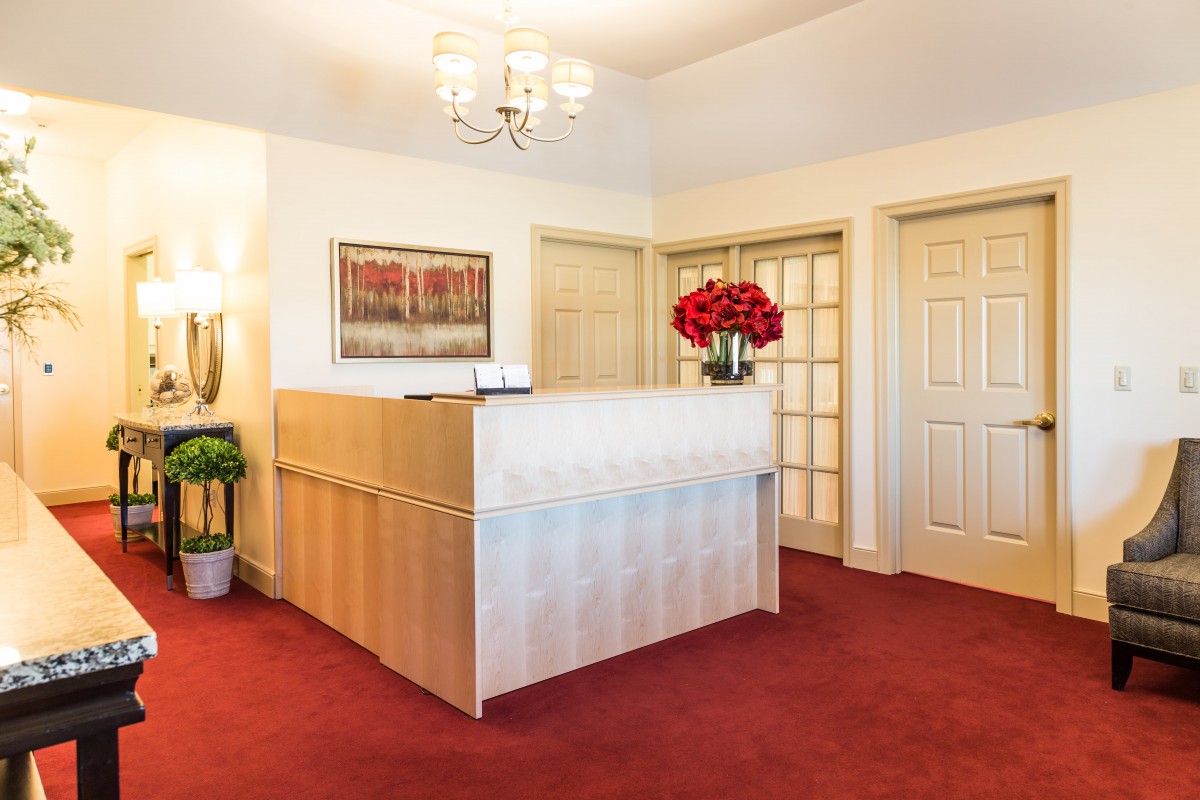 A welcoming reception area with a desk adorned with flowers, carpeted flooring, and artwork on the wall.
