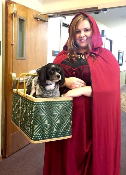 A person dressed as Red Riding Hood carrying a dog in a basket.