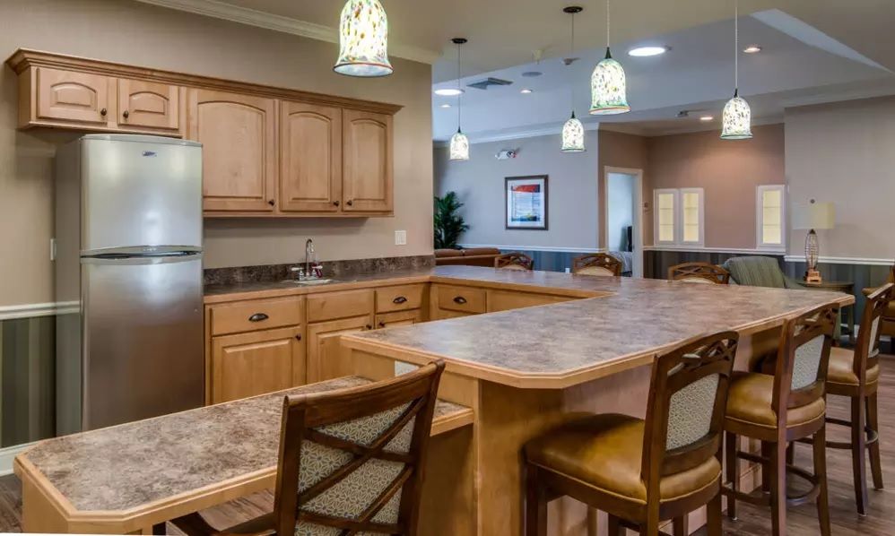 A modern kitchen with wooden cabinets and a marble countertop, featuring pendant lights and bar stools.