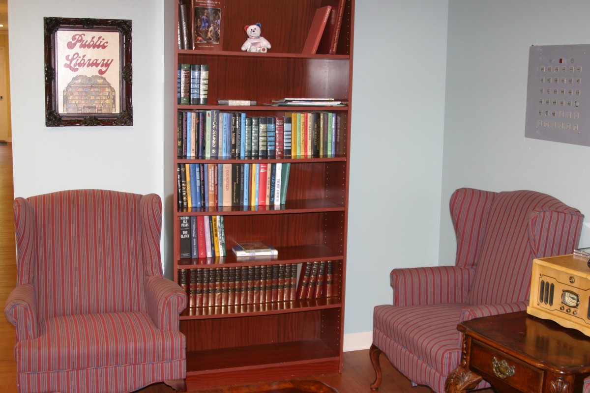A cozy reading nook with a wooden bookshelf filled with books and two comfortable armchairs.