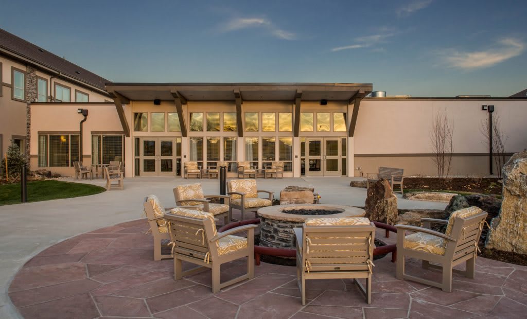A modern patio with comfortable outdoor seating and a central firepit, set against the backdrop of a contemporary building.