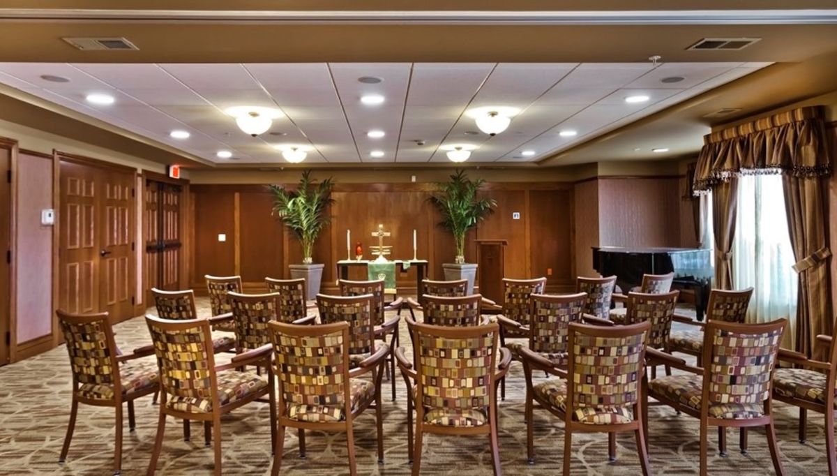 An indoor auditorium with rows of patterned chairs facing a podium, decorated with plants and soft lighting.