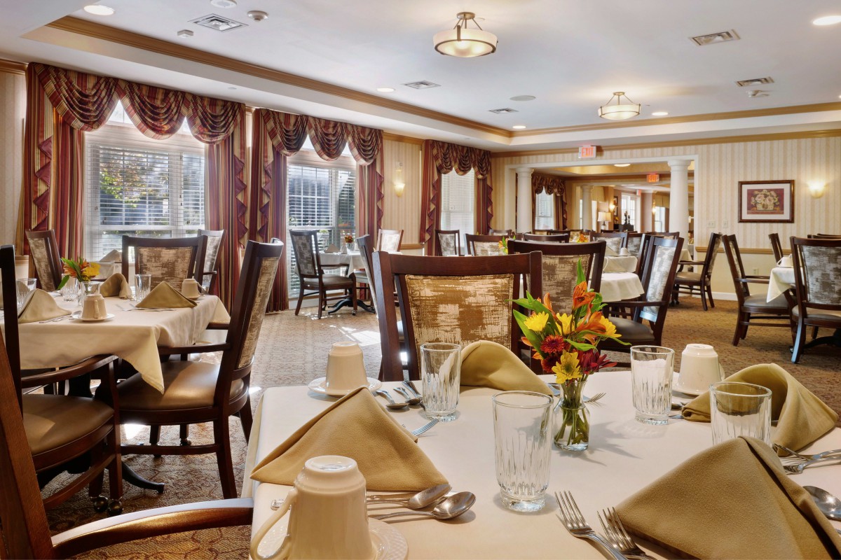 An elegantly set dining area with neatly arranged tables and chairs, featuring floral centerpieces.
