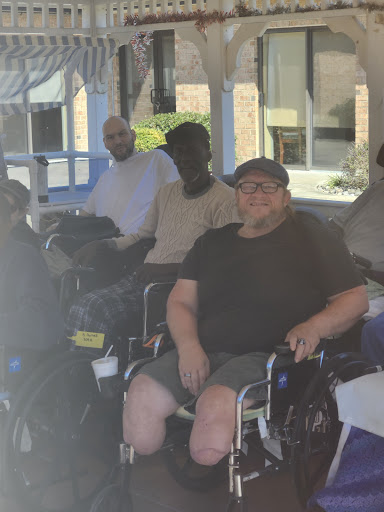 A group of individuals enjoying a sunny day outdoors, gathered in wheelchairs.