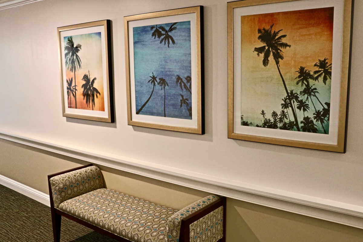 A hallway featuring framed artwork of palm trees above a patterned bench.
