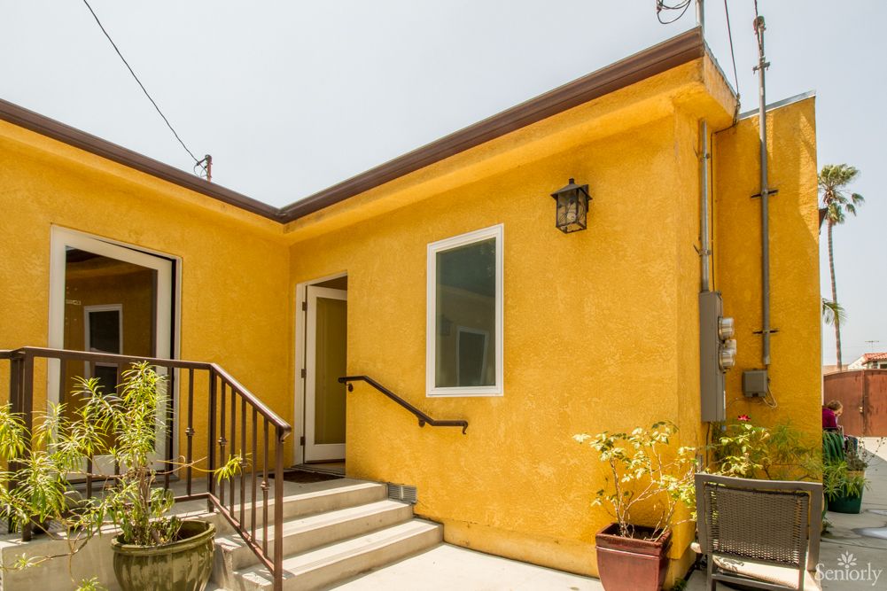 A small yellow stucco house with steps leading to the entrance, featuring potted plants and a lantern.