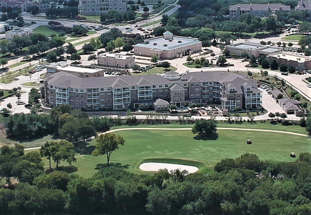 Aerial view of a residential complex adjacent to a golf course surrounded by greenery.
