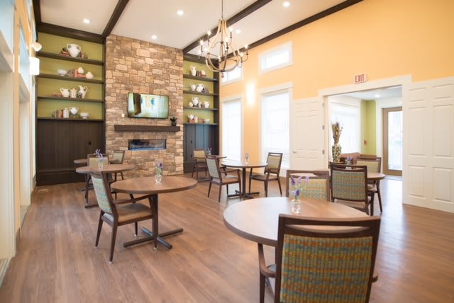 A modern dining area with wooden tables, upholstered chairs, a stone fireplace, and a chandelier.