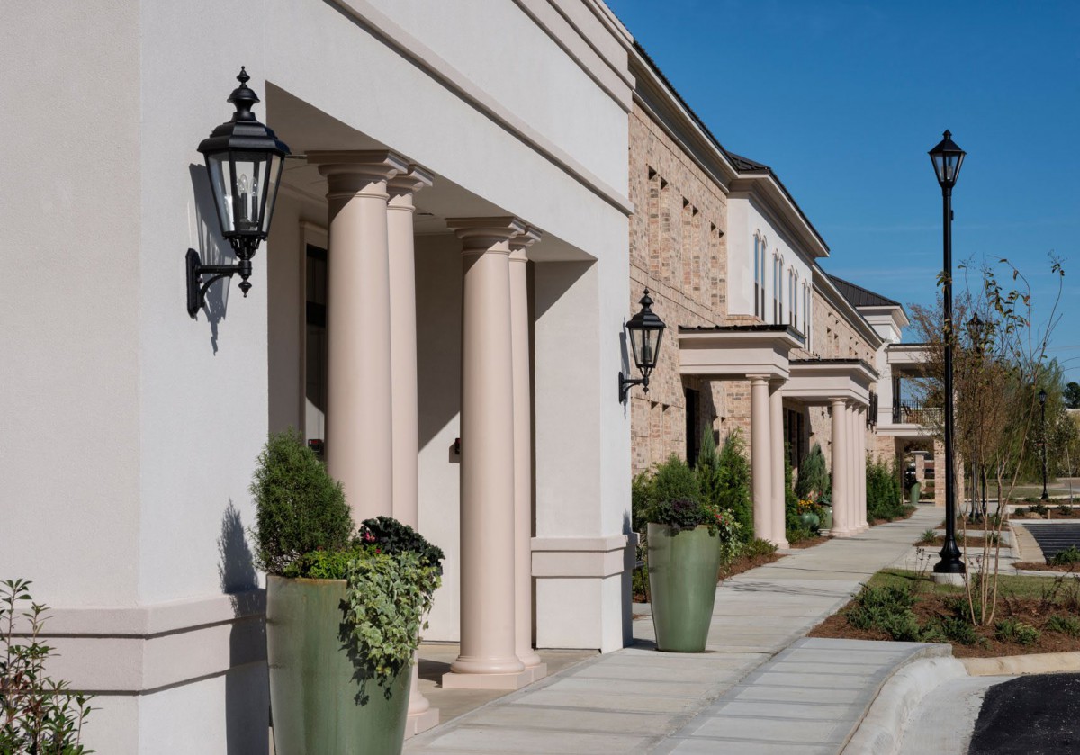 A row of buildings with classical columns and decorative lamps flanking a sidewalk on a sunny day.