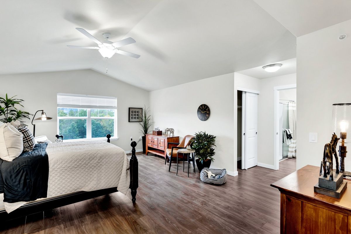 A spacious bedroom with wooden flooring, featuring a bed, ceiling fan, and stylish decor.