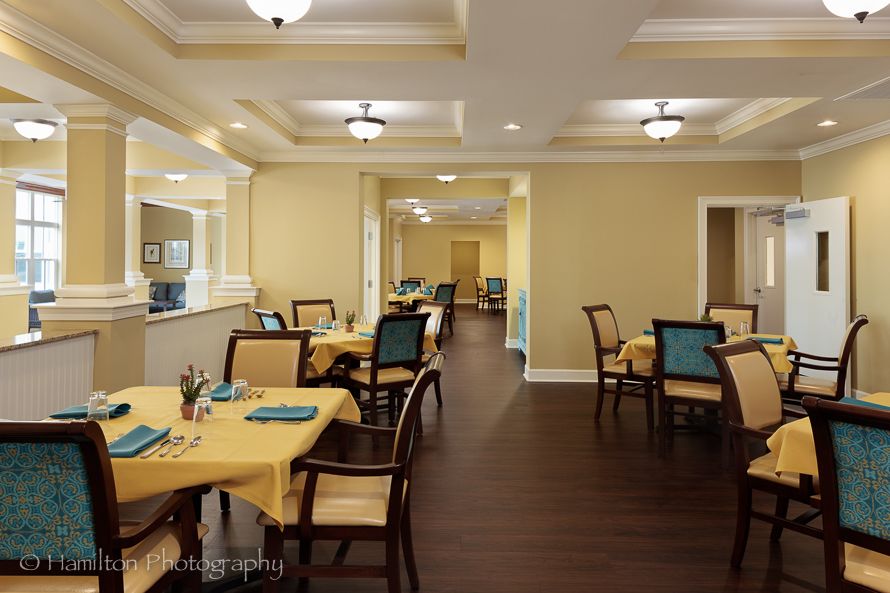 A well-lit dining room with neatly arranged tables and chairs, featuring yellow tablecloths and modern lighting.