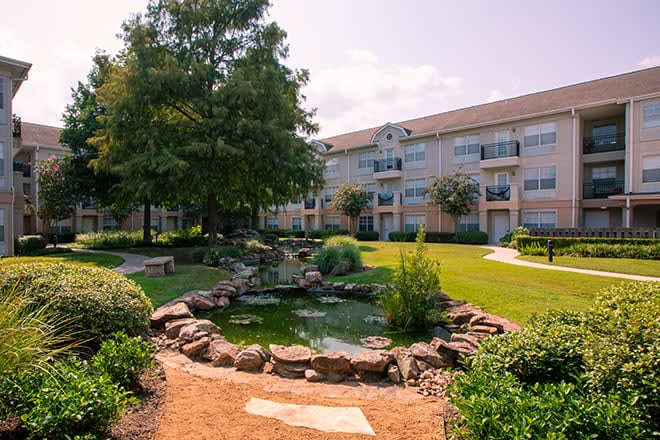 A beautifully landscaped apartment complex featuring a serene pond and lush greenery.
