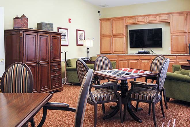 A cozy living room featuring a table with a checkers board, surrounded by chairs and an entertainment center with a TV.
