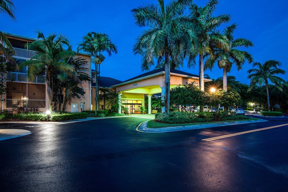 A well-lit hotel entrance at night surrounded by palm trees.