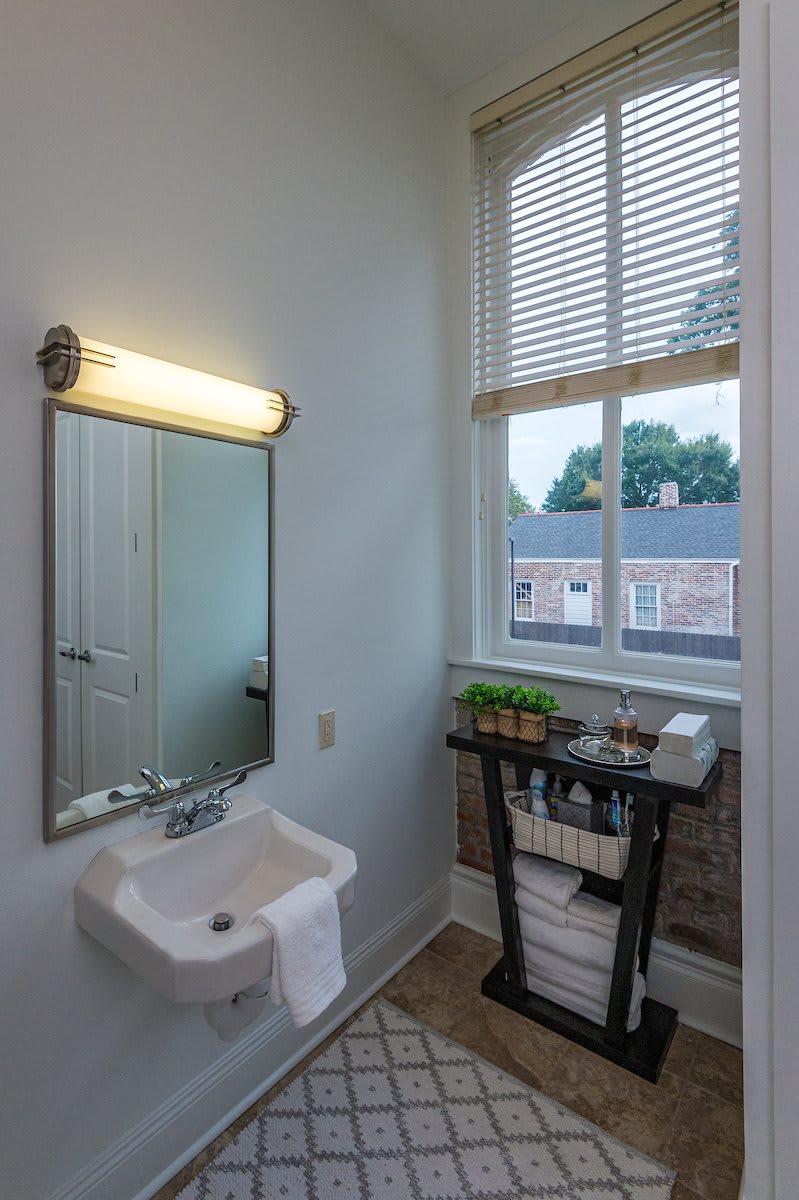 A small bathroom with a sink, mirror, and window overlooking a building.