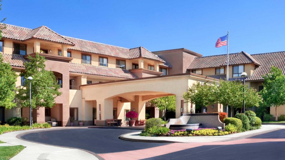 The front entrance of a hotel with landscaped surroundings and an American flag.