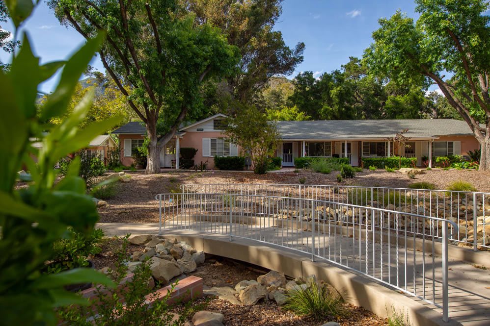 A serene house surrounded by lush trees, featuring a small bridge in the garden.