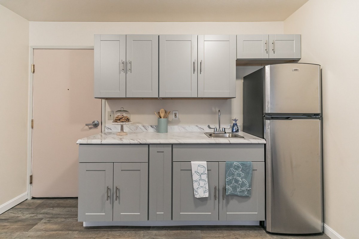 A modern kitchen with gray cabinets, a countertop with utensils and towels, and a stainless steel refrigerator.