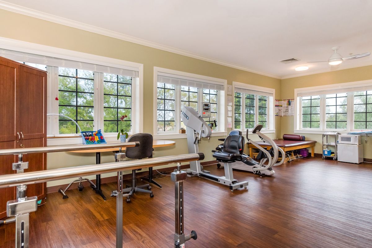 A well-lit rehabilitation gym with exercise equipment and large windows.