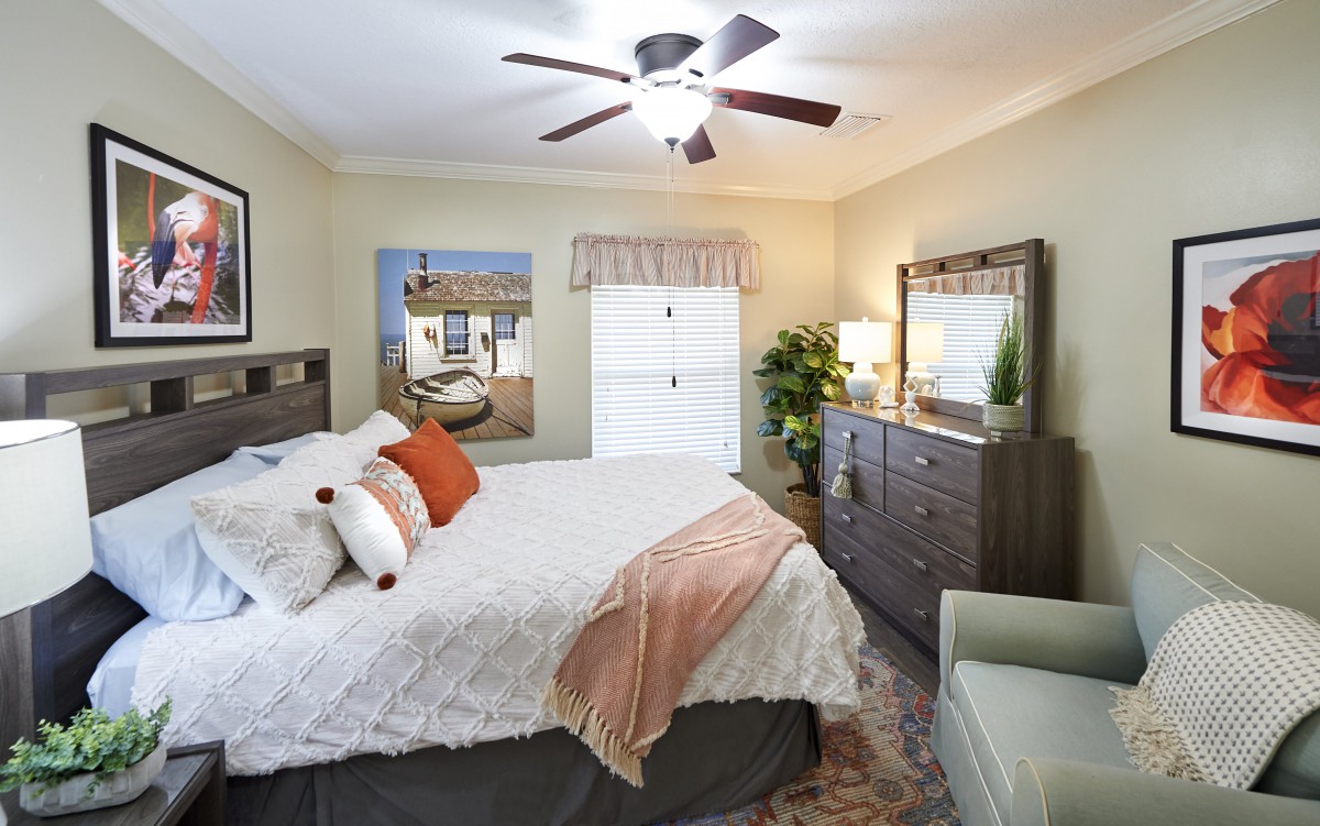 A cozy bedroom with a bed, dresser, and ceiling fan, featuring warm decor and stylish furnishings.
