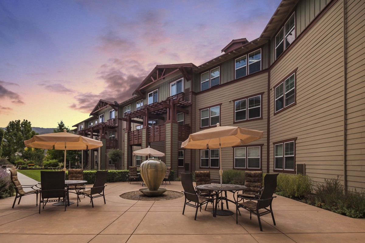A view of a modern apartment building with a well-furnished courtyard at sunset.