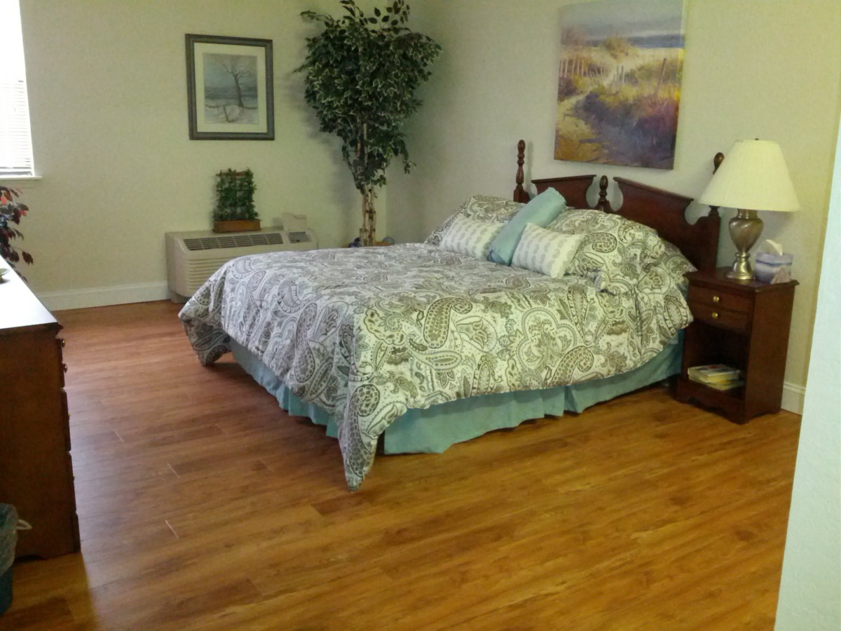 A cozy bedroom with a large bed, decorative pillows, hardwood flooring, and wall art.