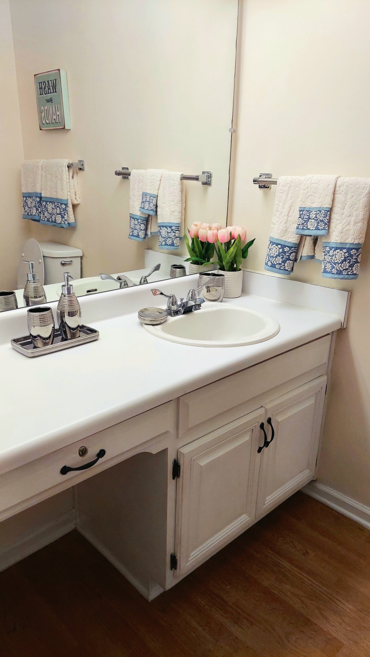 A neatly organized bathroom with a white countertop, sink, mirror, and decorative towels and flowers.