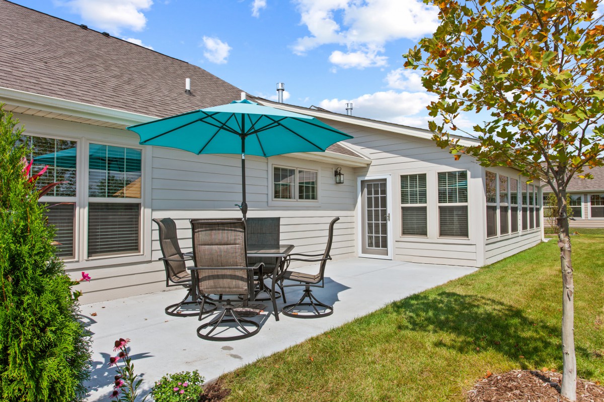 A cozy backyard patio with table, chairs, and a large umbrella under a clear blue sky.