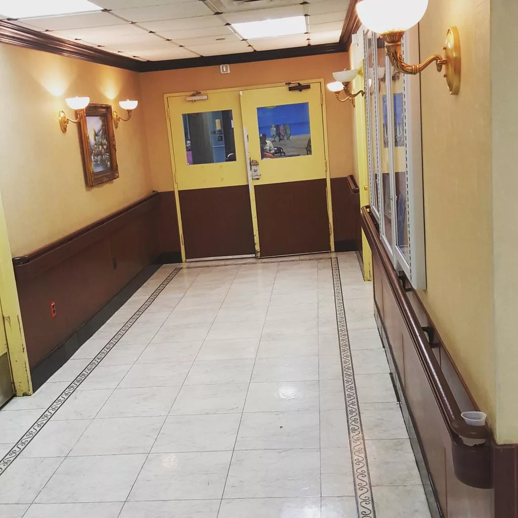 An empty hallway with tiled floors and wall lights leading to double doors.