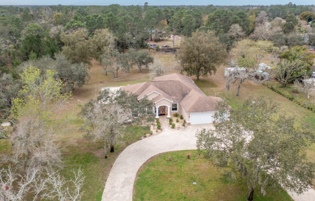 Aerial view of a house with a curved driveway surrounded by trees.
