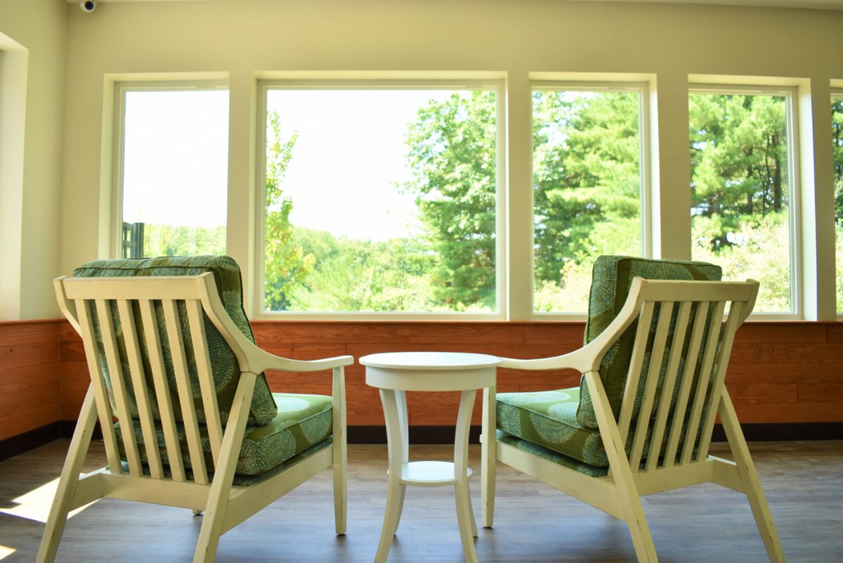A peaceful sitting area with two chairs and a table overlooking lush greenery through large windows.