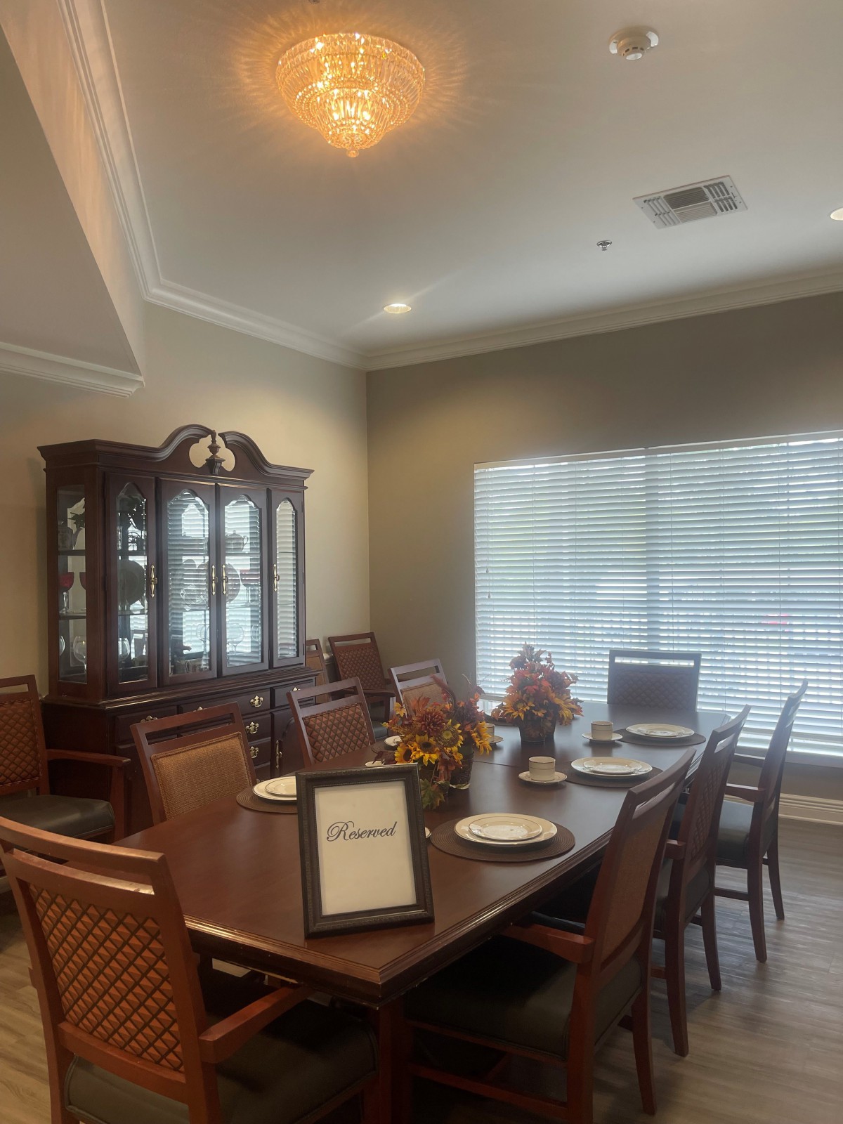 A cozy dining room setup with a large table set for a meal, surrounded by chairs and illuminated by natural light from the window.