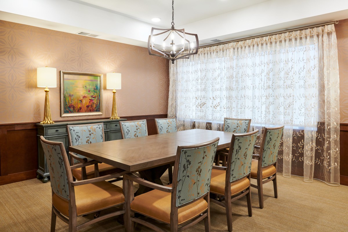 A formal dining room with a wooden table and chairs, featuring a chandelier and wall art.