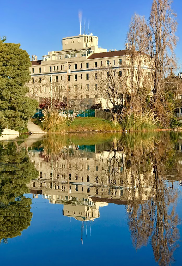 A large building reflected in a calm lake amidst surrounding trees.