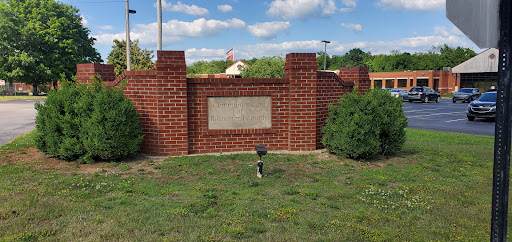 A brick wall with a plaque surrounded by well-maintained grass and bushes under a partly cloudy sky.