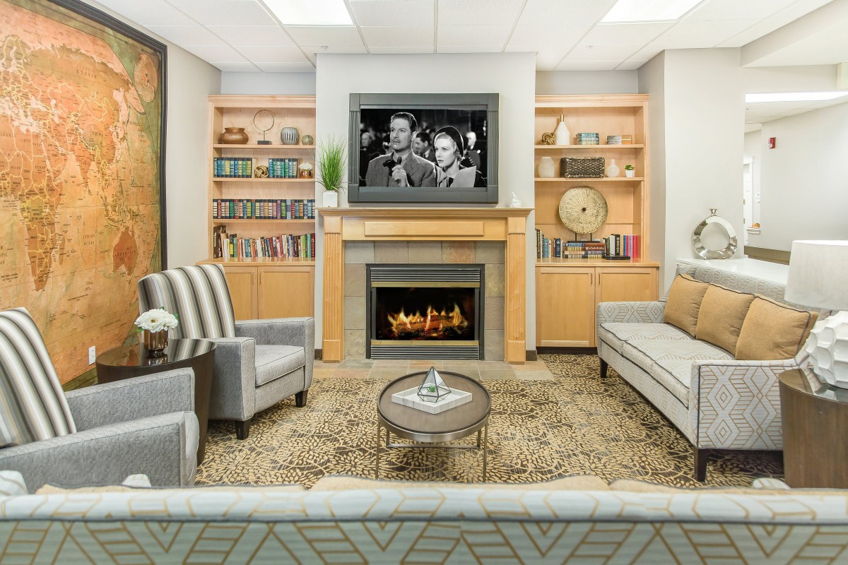 A modern living room with a cozy fireplace and a television mounted above it, surrounded by bookshelves and comfortable seating.