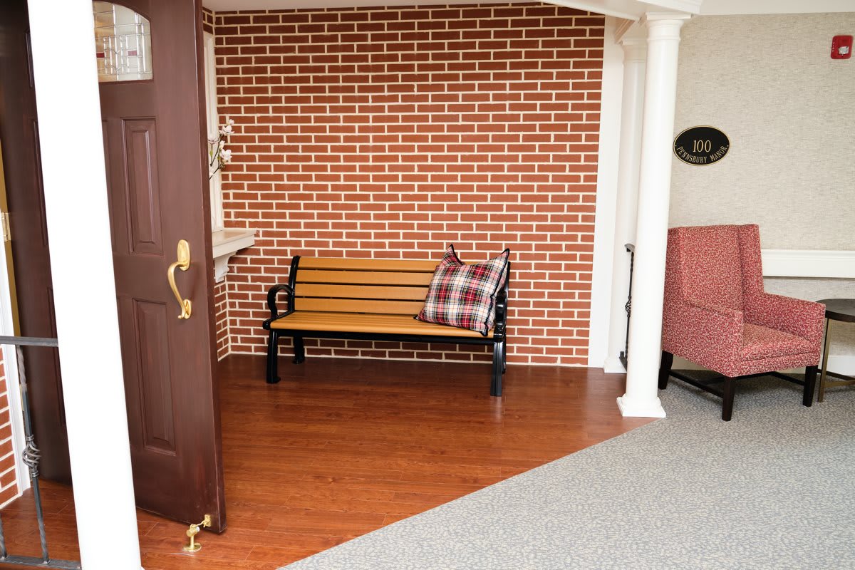 A cozy indoor space with a bench against a brick wall, featuring a decorative pillow on wooden flooring.