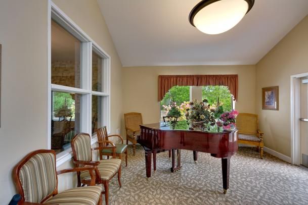 A cozy room with a grand piano, surrounded by elegant chairs and large windows.