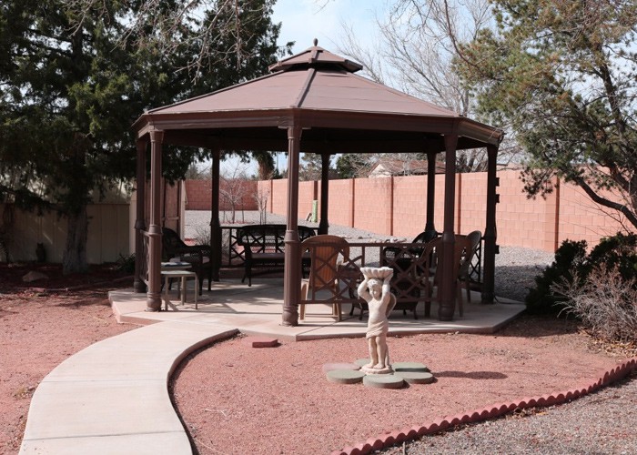 A wooden gazebo in a backyard setting, surrounded by trees and landscaped paths.