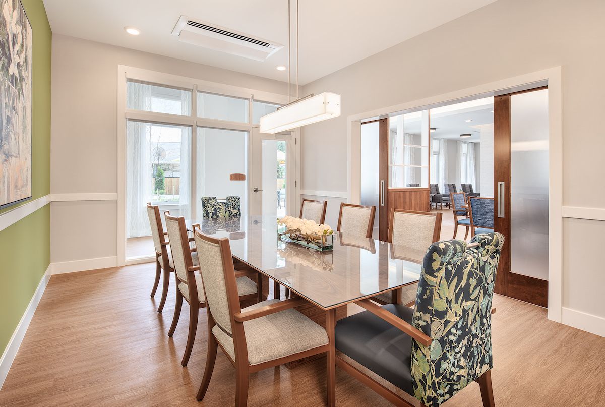 Modern dining room with a large table and chairs, featuring wood flooring and a chandelier.