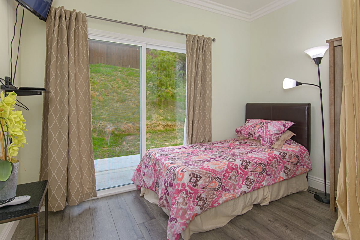 A minimalist bedroom with a single bed featuring floral bedding and large sliding glass doors.