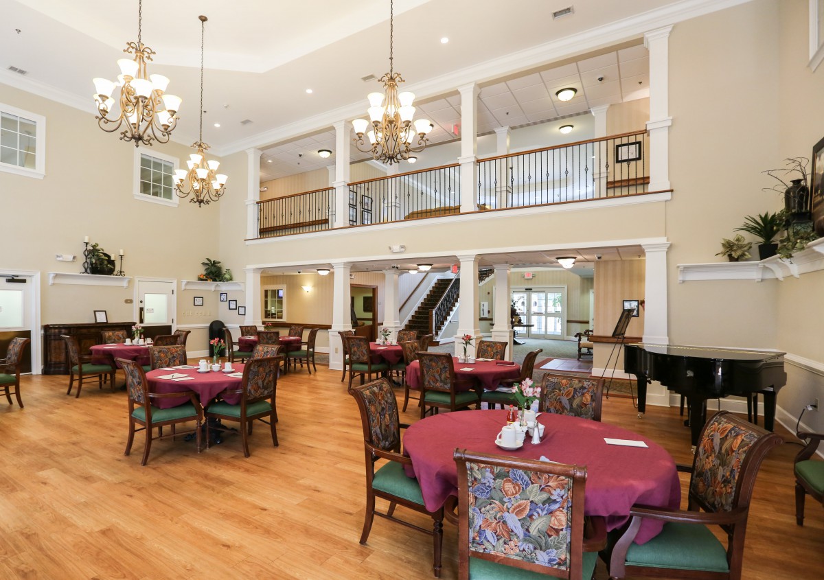 A spacious and elegant dining room with chandeliers, round tables, and intricate chairs.