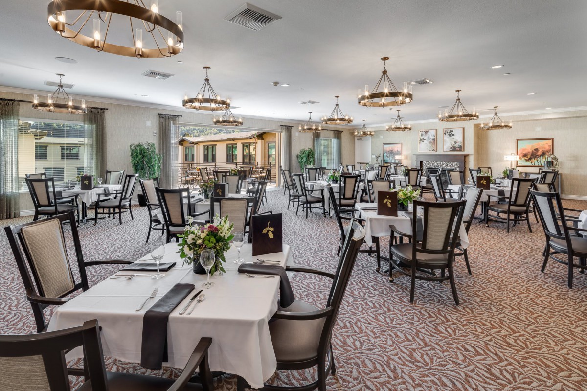 An elegant restaurant dining area with neatly arranged tables and chairs, decorated with chandeliers.
